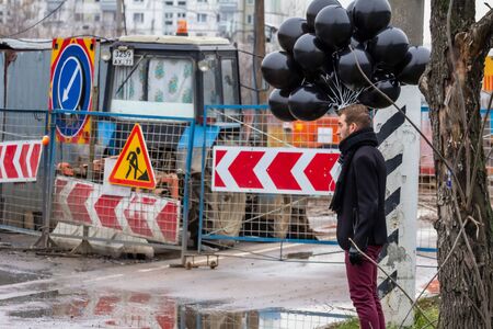 2015.11.22, Moscow, Russia. birthday is a sad holiday concept. A young man wearing black scarf and coat holding black balloons on background of urban scene, blur and grain effect.のeditorial素材