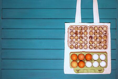 set of quail and chicken eggs and white cotton bag on a blue wooden background