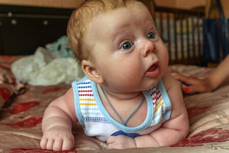 newborn boy lies on his stomach on the bed and looking away. baby boy in the early days of home.