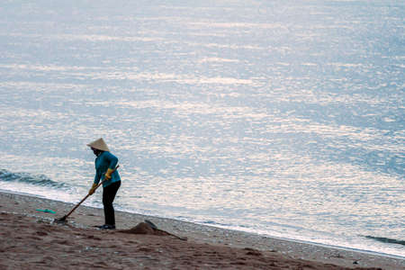05/02/2015, Phan Thiet, Vietnam. Vietnamese worker in a national hat cleans the trash from the beach...