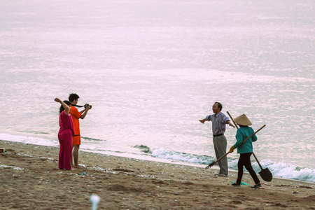 05/02/2015, Phan Thiet, Vietnam. Vietnamese worker in a national hat cleans the trash from the beach in the early morning.のeditorial素材