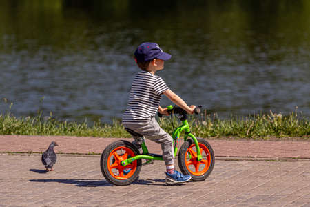 05/26/2018, Moscow, Russia. A little fashionably dressed boy rides on a runbike along the river in the park. Active lifestyle of kids.のeditorial素材
