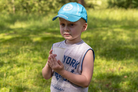 06.24.2020, Maloyaroslavets. Russia. A little boy eating berries from plastic cup. Dinner on the open air.のeditorial素材