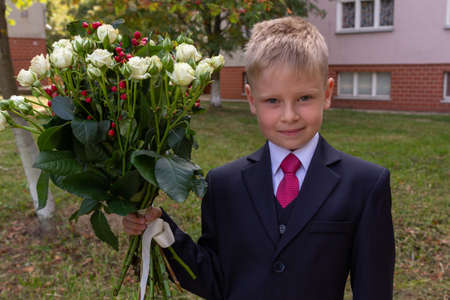 Portrait of a blond boy dressed in a classic suit and holding a bouquet of roses, looking to camera. First grader going to go to school.の写真素材