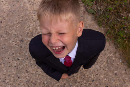 Portrait of a blond first-grader boy dressed in a dark suit with his arms outstretched to the camera, view from above. A boy having fun.の写真素材