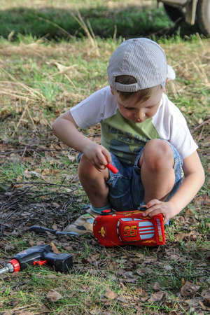 04/29/2012, Maloyaroslavets, Russia. little boy repairing a toy car. A kid playing on the open air.のeditorial素材