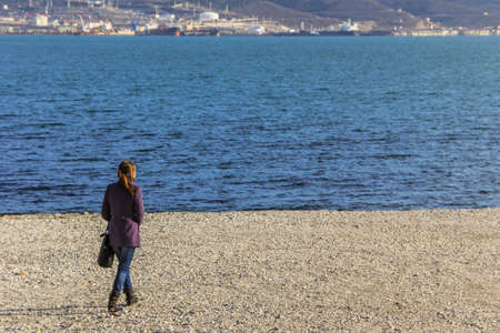 12/09/2012, Novorossiysk, Russia. A young long haired woman walking along the coast of the sea on background of mountains.のeditorial素材