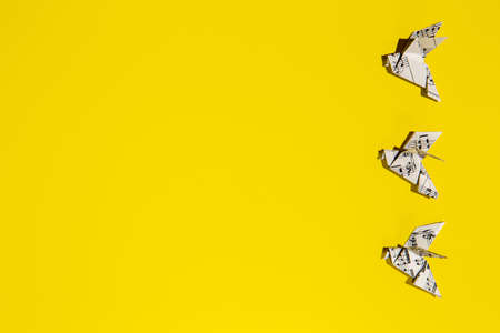 Flock of flying origami doves on yellow background. Origami bird's group from music paper. Concept of festive music postcard.の写真素材