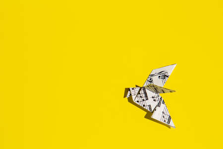 Flying origami dove on yellow background. Origami bird from music paper. Concept of festive music...