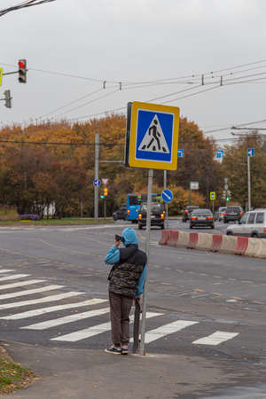 11.10.2020, Moscow, Russia. A teen boy going to cross the road at the crossing. A young man standing by the road sign.のeditorial素材