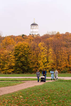 11.10.2020, Moscow, Russia. People standing under an oak and maple trees against the trunk. People walking around autumn park.のeditorial素材