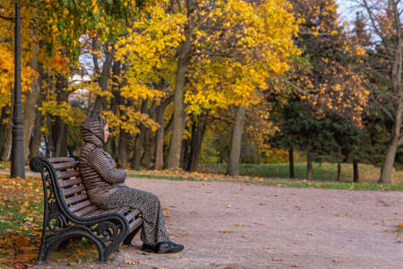 13.10.2020, Moscow, Russia. A single woman sitting on the bench in the autumn park. Sad emotions of adult woman.のeditorial素材