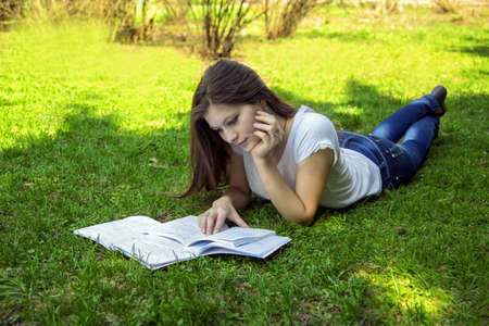 Student woman teaches from notes lying on the grass in the park