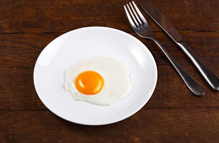 white plate with fried egg on wooden background