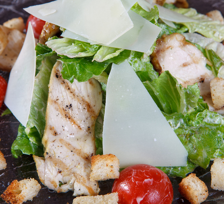 Macro fragment of salad with grilled chicken meat, lettuce, tomatoes and croutons.  Glass dish on a brown woodenの写真素材