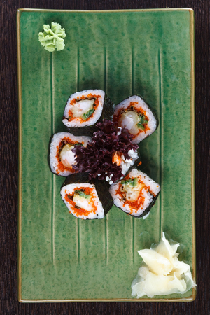 Sushi rolls on a plate with flying fish roe on dark brown wooden table. Side view. の写真素材