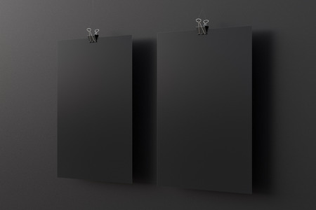 Two blank black paper posters hanging on binder clip on black wall background. 3d illustrationの写真素材