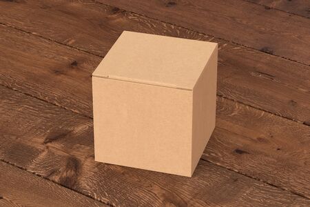 Blank cardboard cube gift box with closed hinged flap lid on dark wooden background.