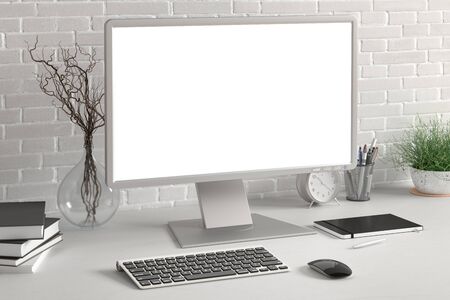 Workspace with blank computer monitor white screen mock up on the white desk near white brick wall. 3d illustrationの写真素材