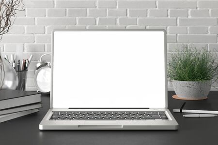 Workspace with blank laptop monitor white screen mock up on the black desk near white brick wall. 3d illustrationの写真素材