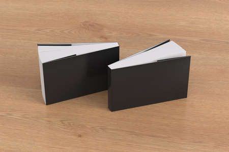 Two softcover or paperback horizontal or landscape black mockup books standing on the wooden...