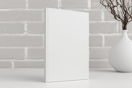 Vertical book cover mock up standing on a white desk with white brick wall background. 3d illustrationの写真素材