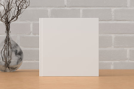 Square book cover mock up standing on a wooden desk with white brick wall background. 3d illustrationの写真素材