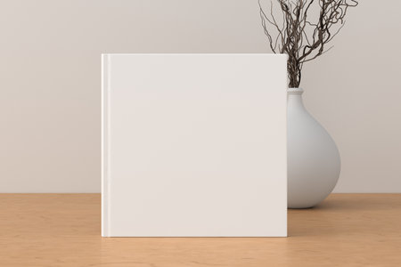Square book cover mock up standing on a wooden desk with white wall background. 3d illustrationの写真素材