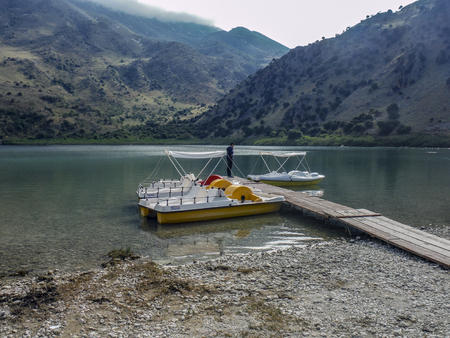 A view of the natural Lake Kournas, recreational boats and mountains around on a cloudy spring day (island Crete, Greeceの写真素材