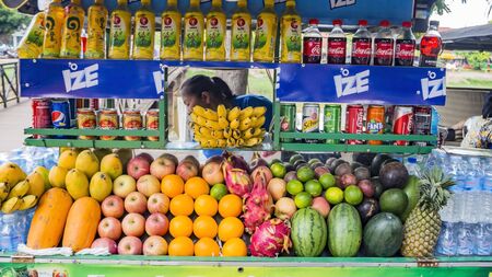 SIEM REAP, CAMBODIA - NOVEMBER 24, 2017:  Asian woman - seller with variety of  fruits including dragon fruit, lychees and carrots, displayed for sale at the open air market. Cola and other drinksのeditorial素材