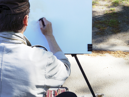 Unfinished ART work. Professional painter at work. Concentrated male artist is drawing a girl on easel, creative atmosphere, real urban scene,  tools paints beside his feetの写真素材