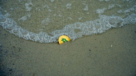 Bitcoin sinks. golden bitcoin crypto currency drop on the beach sand  by the sea at the summer day,...