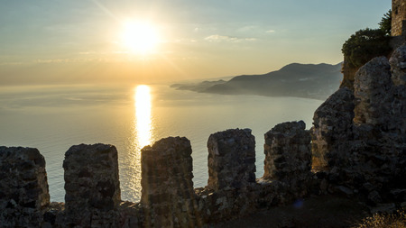 View from the fortress Calais. Sunset at the beach in Alanya, Turkey. View of the castle hill and sea, evening ligh. Mountains and clouds on the background. Copy space. Sun rays and reflectionの写真素材