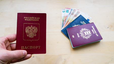 hand holding Passport on the wooden background. Citizenship of Estonia and Russia or European Union (EU) and Russian Federation. side view. Copy space design. Rubles and Euro banknotes.の写真素材