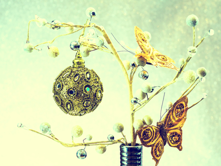 Silver vase. Plant with pearls, golden butterflies. Christmas tree toys, blurred  background. Fir tree. New Year. Lights bokeh. Christmas concept. Copy space. Vintage tone filter effect color style.の写真素材
