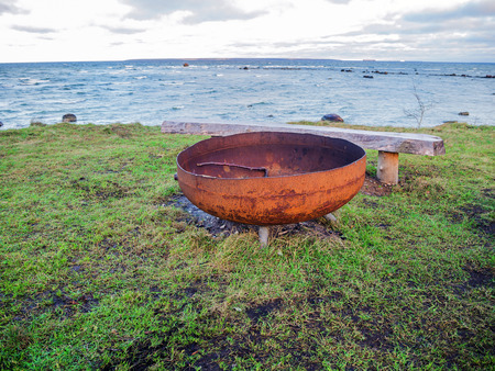Antique Cast Iron Cauldron, Pot Kettle or  rusty Fire Bowl and old wooden bench. Nature conservation area (Tabasalu Nature Park, Baltic sea) with sea stones. Beach meadows with sea salt adherenceの写真素材