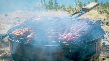 Closeup of grilled sliced sausages, tasty picnic food , sea and nature background. barbecue with...