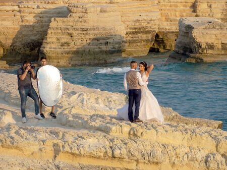 CYPRUS, PAPHOS ? SEPTEMBER 14, 2019. Bride on a stone bridge in the sea. married hugging on a background the sea with a wedding bouquet. Sunset, Slow motionのeditorial素材