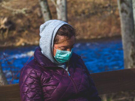 Lady and coronavirus protection. Sad Woman sitting alone on bench in park wearing mask to avoid...