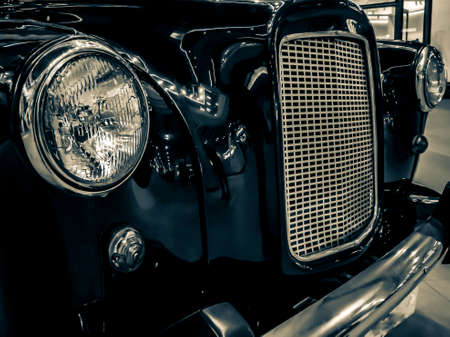 TALLINN, ESTONIA- SEPTEMBER 19, 2019: Front view of a black retro car. Black old car with headlamp and chrome radiator grill. Photo of a headlight of a Classic vintage retro automobile. Filtered imageのeditorial素材