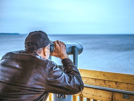 man looking through tourist binoculars. Hands on the telescope. ocean on the background. vacation...