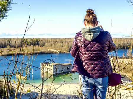 Hiker on mountain top with smartphone. Woman is standing and taking a picture on smartphone. Abandoned Quarry Of Rummu, Estonia. Scenic View Of Land Against Clear Blue Sky. Panoramic View. の写真素材