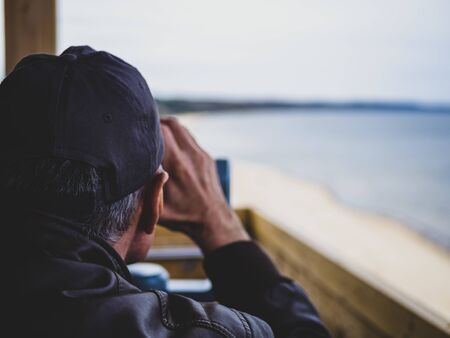 man looking through tourist binoculars. Hands on the telescope. ocean on the background. vacation conceptの写真素材