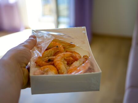 paper packaging filled with fresh shrimps in man hands. window on the blurred background. Food for diet - Grilled shrimps with mango salad. Home cook in Asian kitchen.の写真素材