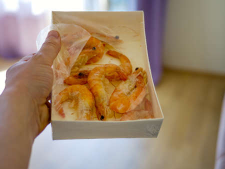 paper packaging filled with fresh shrimps in man hands. window on the blurred background. Food for diet - Grilled shrimps with mango salad. Home cook in Asian kitchen.の写真素材