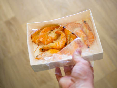 paper packaging filled with fresh shrimps in man hands. brown floor on the blurred background. Food for diet - Grilled shrimps with mango salad. Home cook in Asian kitchen.の写真素材