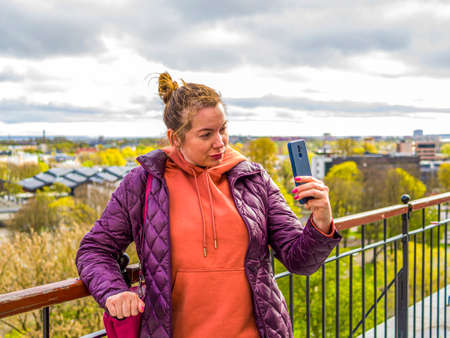 Tourist in Estonia, taking photo of old town with smartphone. Travel photography with mobile phone. travel and photography concept, young beautiful woman in red looks towards city towers. copy spaceの写真素材