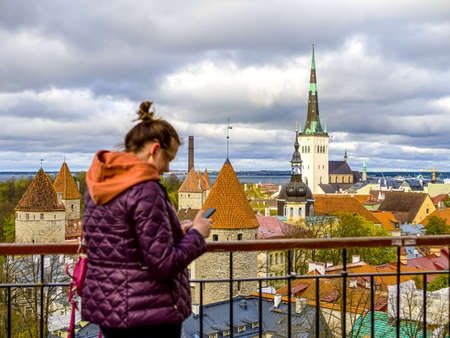 Tourist in Estonia, taking photo of old town with smartphone. Travel photography with mobile phone. travel and photography concept, young beautiful woman in red looks towards city towers. copy spaceの写真素材