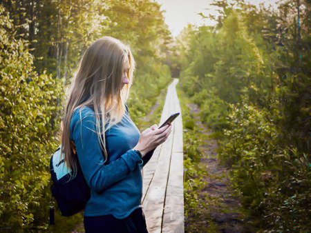 view of beautiful woman traveler standing in forest, Estonia. lifestyle tourist girl backpack standing with smartphone , explorirng directions. Vacation concept, summer time. Toned image. Sunsetの写真素材