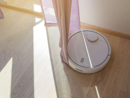 Robotic vacuum cleaner cleans the room from dust and debris, light from the window, technological progress. Robotic vacuum cleaner eats the curtains. Error concepts. Filtered image with copy spaceの写真素材